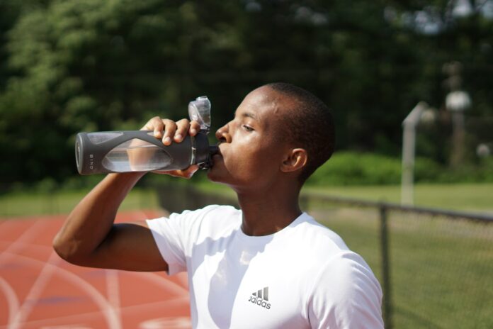Photo by Nigel Msipa man in white crew neck t-shirt drinking from black sports bottle